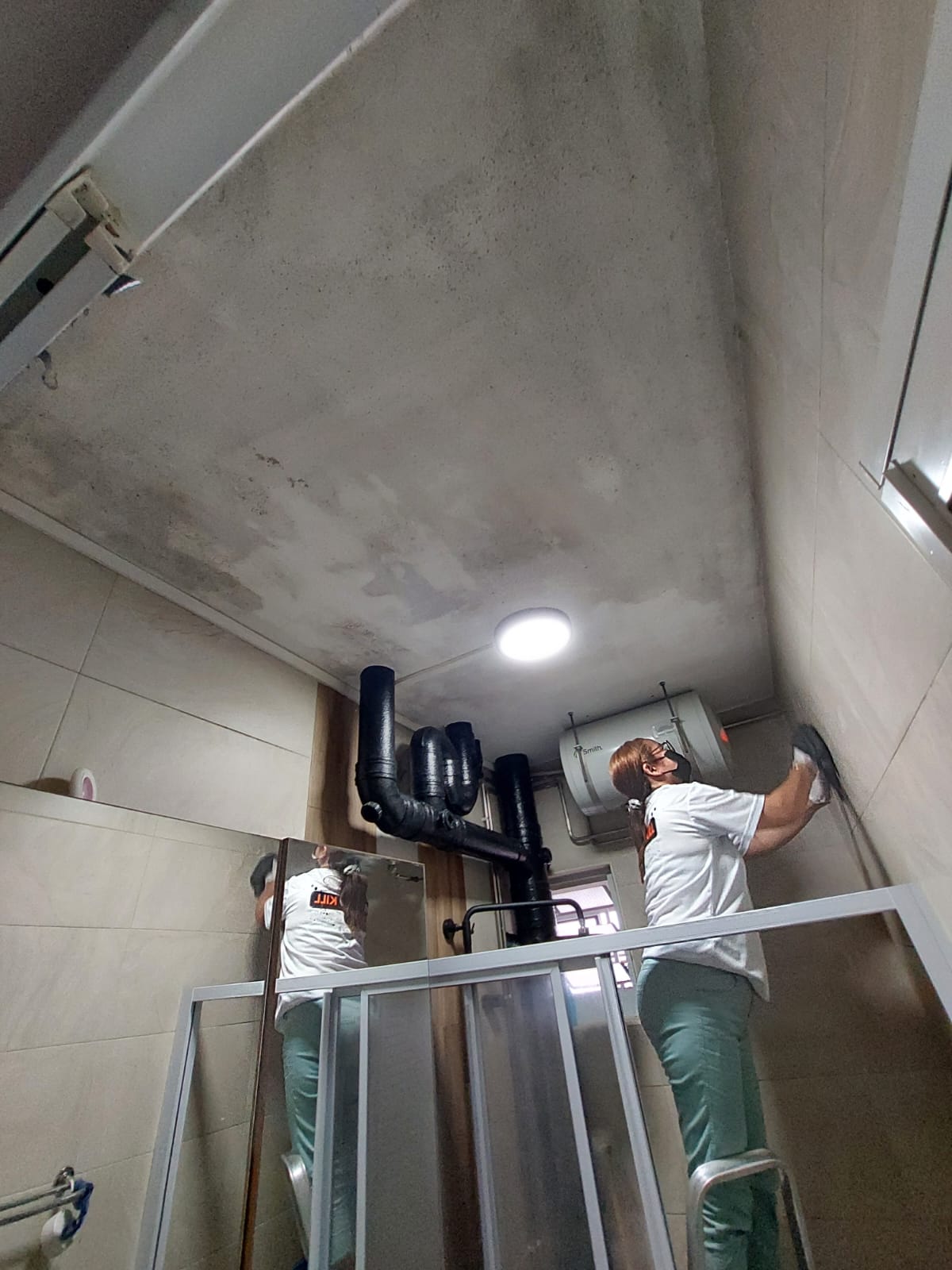 Technician wiping mould from a bathroom ceiling and wall in a Singapore flat before repainting