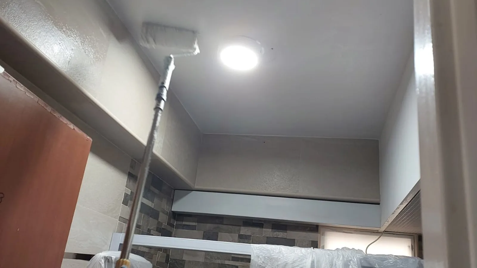 Technician roller-painting a bathroom ceiling with anti-mould paint after treatment in a Singapore home