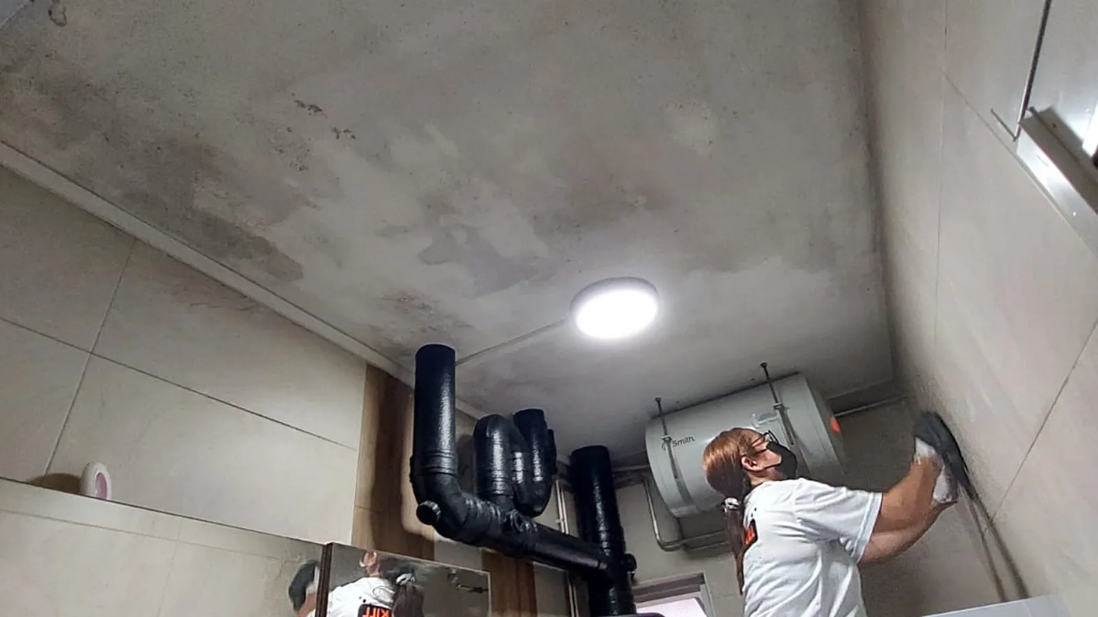 Technician wiping mould from a bathroom ceiling and wall in a Singapore flat before repainting