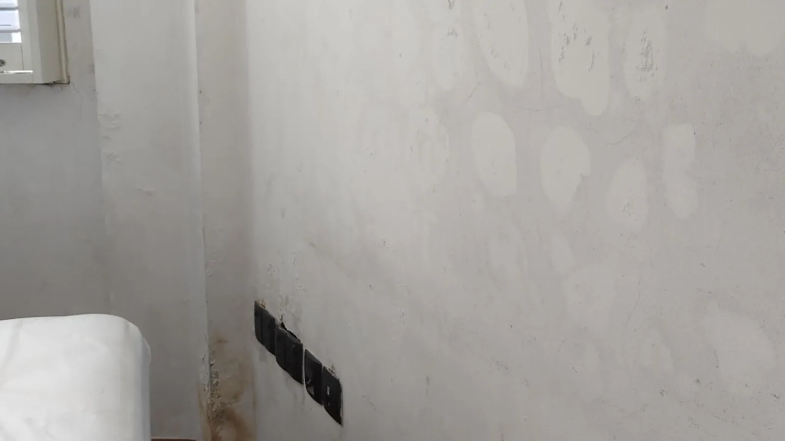 Bedroom wall in a Singapore home with mould patches and skirting damage behind furniture near a window