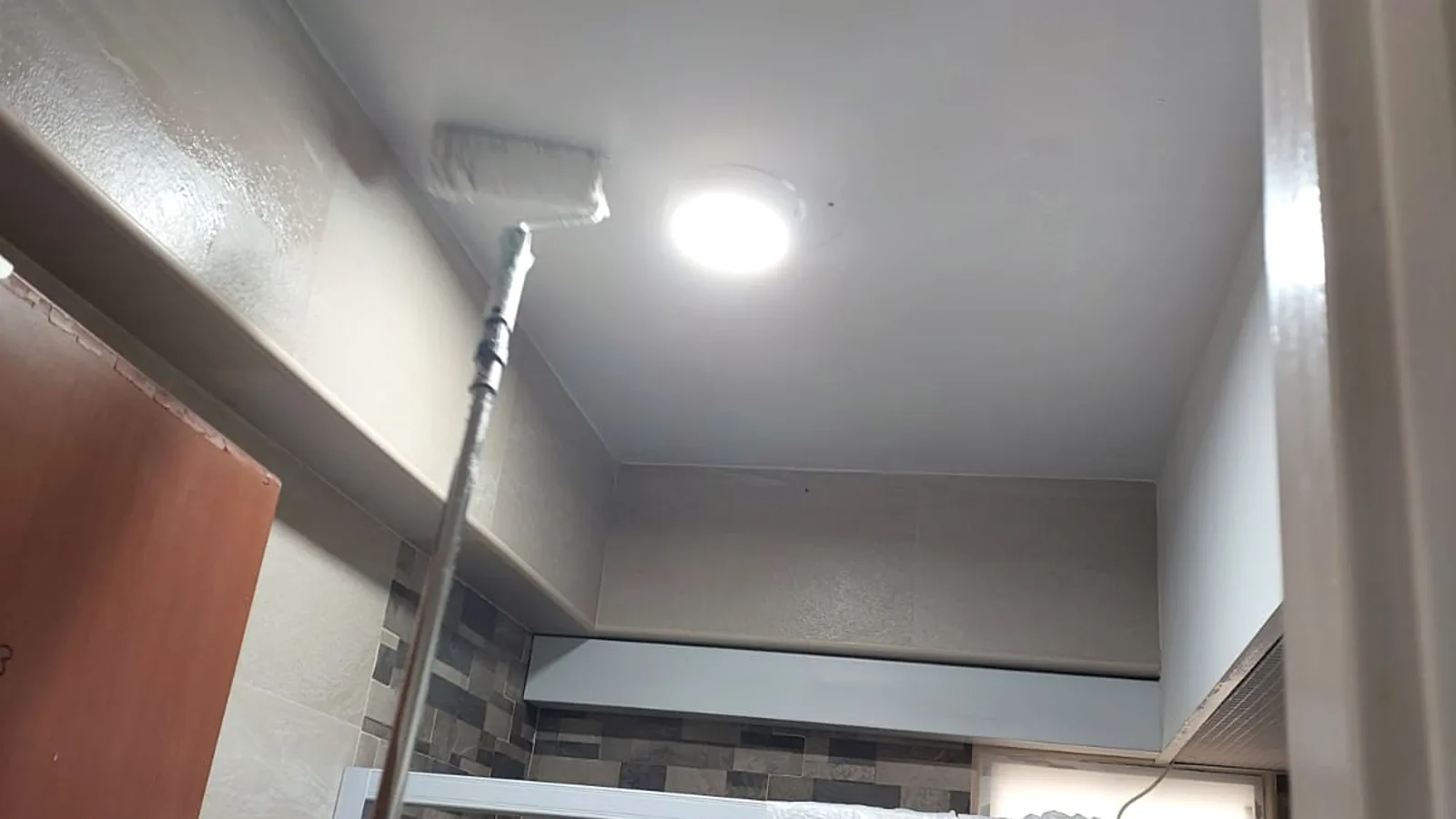 Painter rolling fresh paint across a treated Singapore bathroom ceiling, finishing the mould-resistant protection.