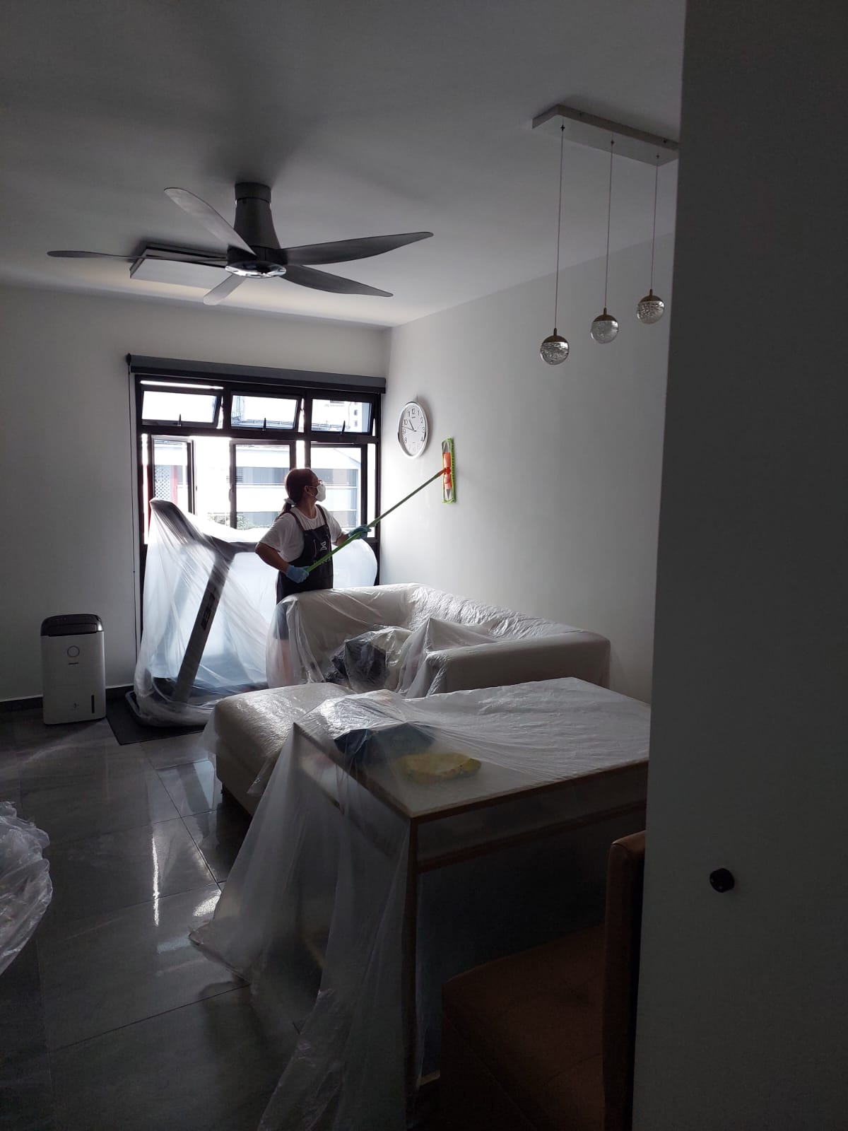 Technician treating a living room wall with furniture protected under plastic sheeting in a Singapore flat