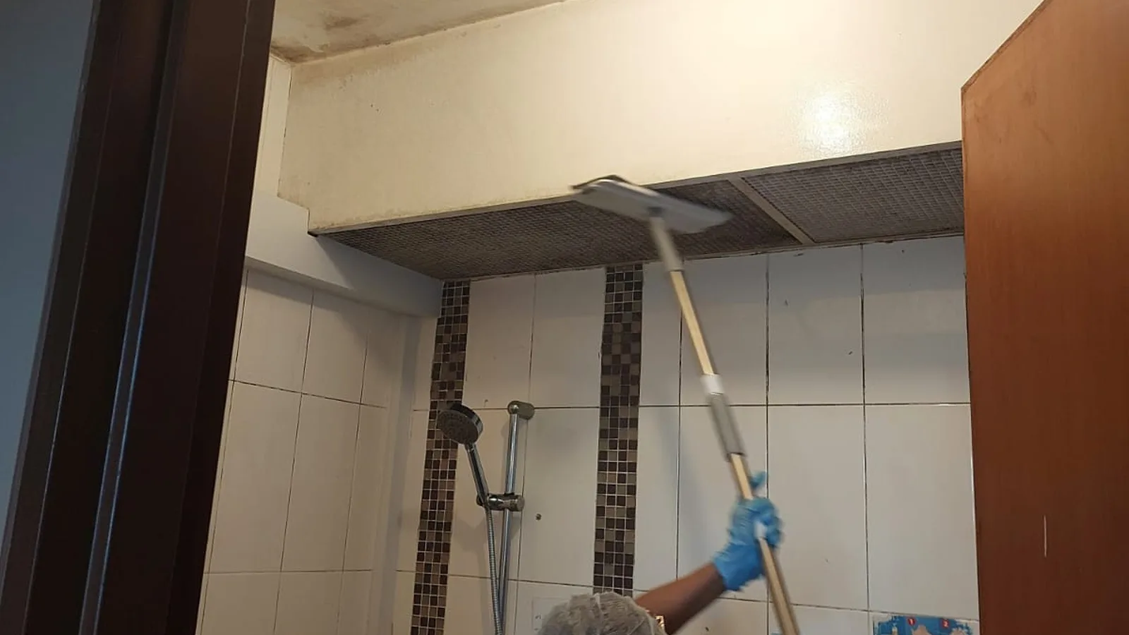 Technician in gloves and hair cover cleaning a bathroom ceiling with a long pole in a Singapore home