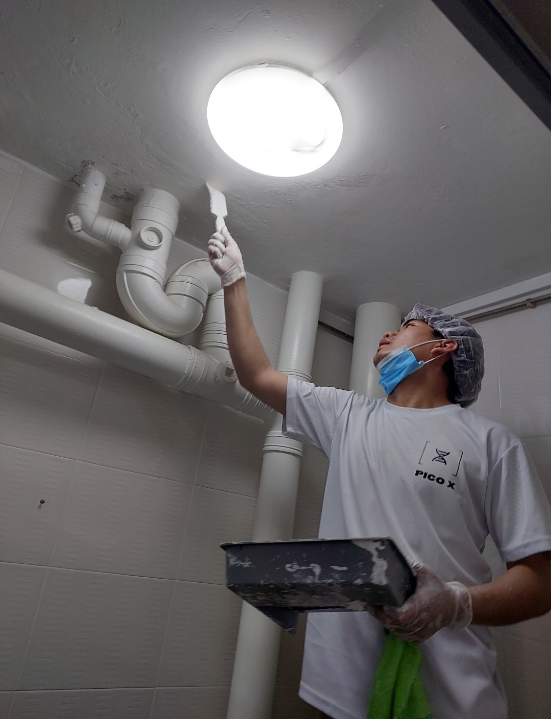 Pico X Health technician applies anti-mould paint to bathroom ceiling and pipes in protective gear - Singapore HDB