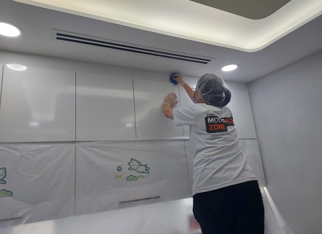 Pico X Health technician applies anti-mould treatment to kitchen cabinet area with ceiling AC in full PPE - Singapore